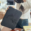 A black ultra-thin laptop sleeve case is held by a person, resting on a wooden surface.