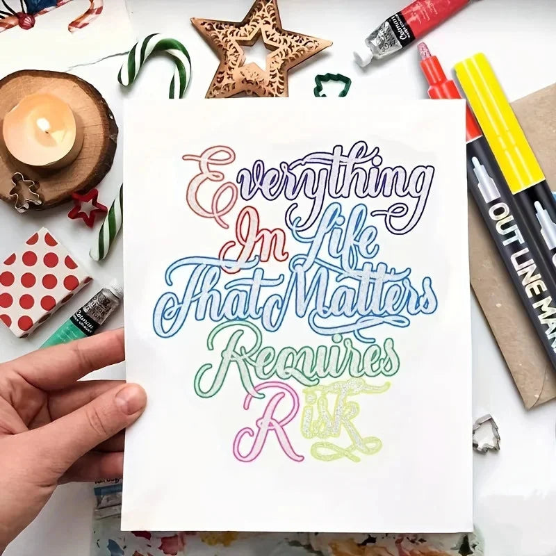 A hand holds a sheet of paper with colorful script writing on it, surrounded by art supplies.