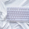 A close-up shot of white custom profile keycaps for a mechanical keyboard resting on draped white fabric.