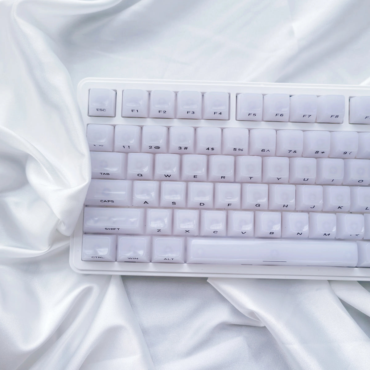 A close-up shot of white custom profile keycaps for a mechanical keyboard resting on draped white fabric.