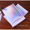 A stack of iridescent rainbow foil bubble mailers for gifts and documents resting on a wooden surface.