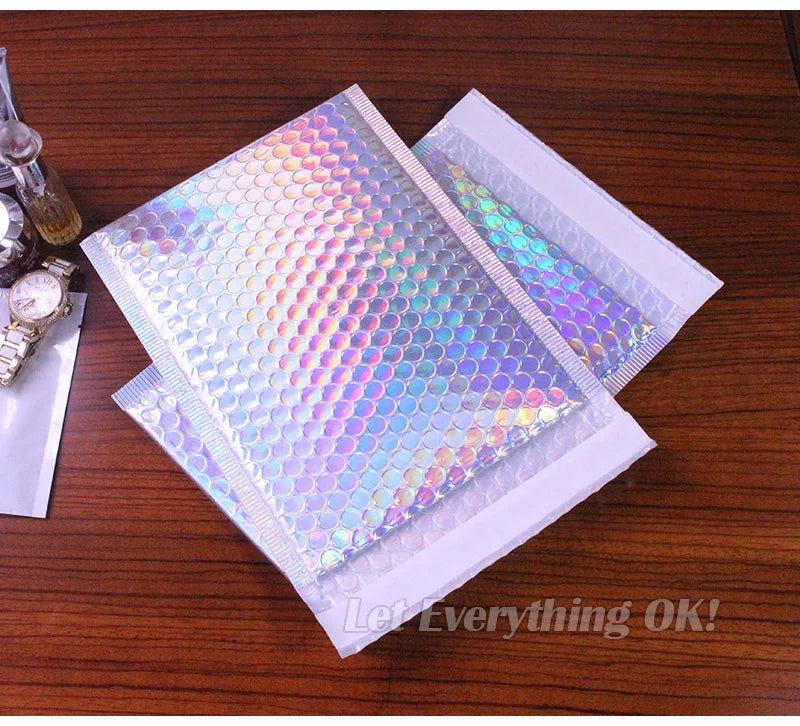 A stack of iridescent rainbow foil bubble mailers for gifts and documents resting on a wooden surface.