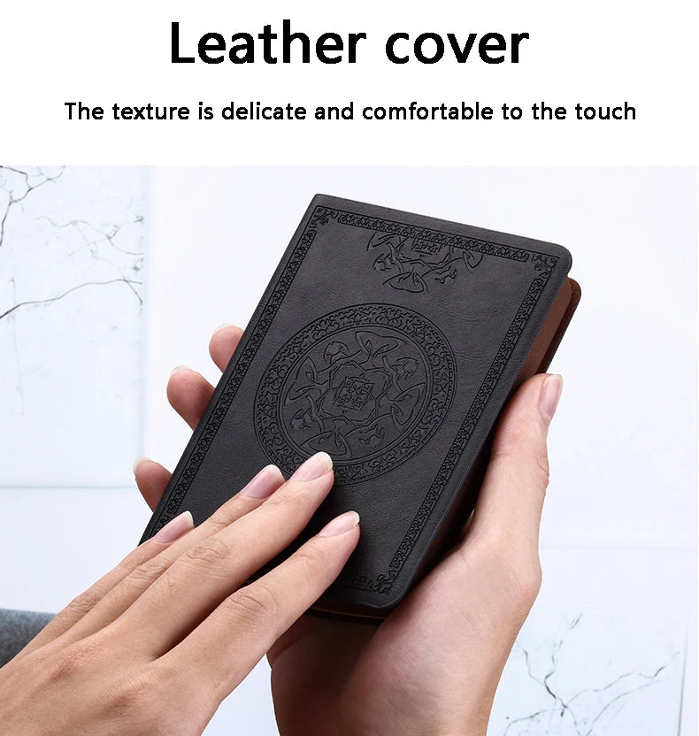 A hand holds a black leather cover notebook with an embossed design.