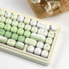 A close-up view of a light green and white PBT keycap set with MOG profile keys resting in a light colored plastic case.