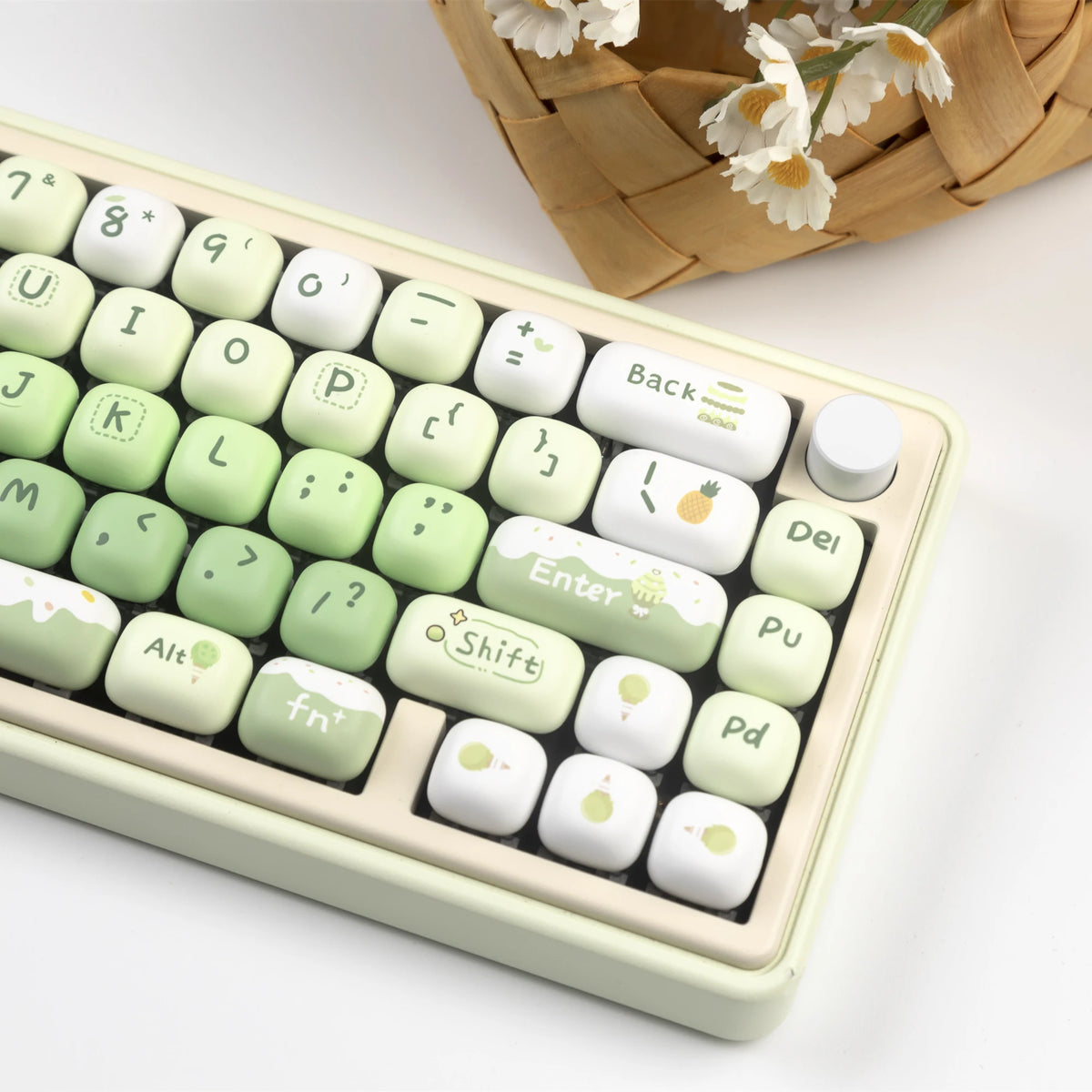 A close-up view of a light green and white PBT keycap set with MOG profile keys resting in a light colored plastic case.