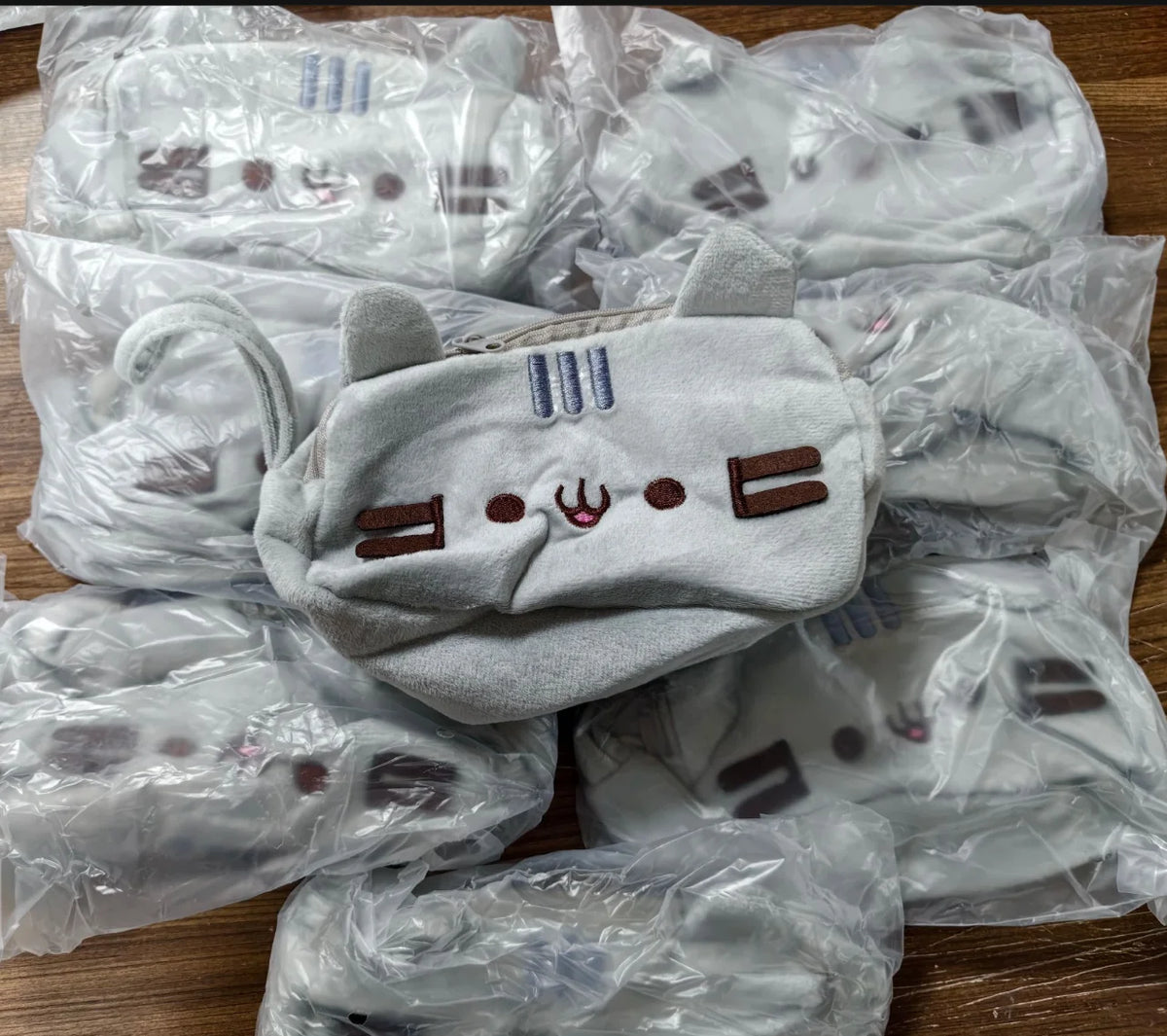 A pile of light gray plush cat pencil cases for stationery, packaged in clear plastic bags.