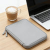 A gray waterproof PU leather laptop sleeve resting on a wooden table next to a cup of coffee and a silver laptop.