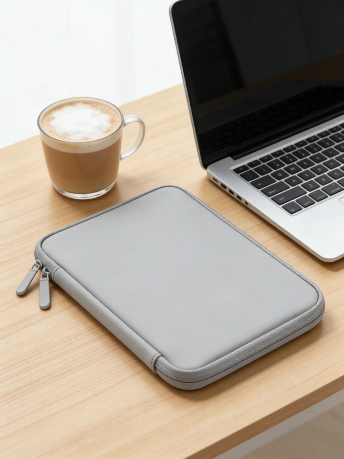 A gray waterproof PU leather laptop sleeve resting on a wooden table next to a cup of coffee and a silver laptop.