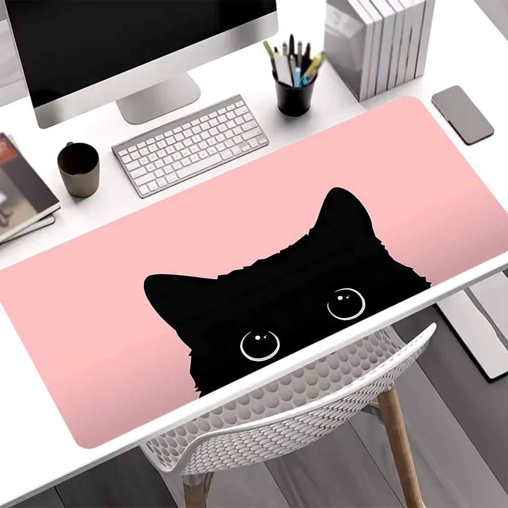 A pink mouse pad featuring a black cat face is placed on a white desk next to a computer and stationery.