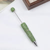 A silver pen accessory featuring a green rhinestone bead and a textured body.