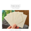 Una mano sostiene una pila de sobres de papel kraft beige claro para invitaciones de boda.