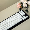 A close-up view of a black mechanical keyboard with white keycaps and a bouquet of pink and white roses.