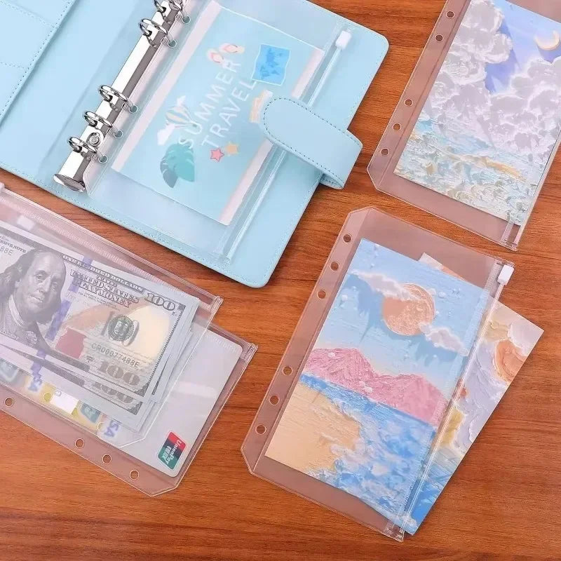A set of clear plastic zippered envelopes and a light blue notebook featuring summer travel themes.