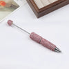A silver pen accessory with a pink rhinestone tip and decorative beadwork is shown on a white background.