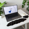 A black ergonomic memory foam wrist rest pad is placed on a white desk next to a laptop and mouse.