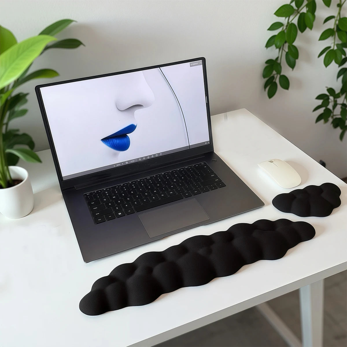 A black ergonomic memory foam wrist rest pad is placed on a white desk next to a laptop and mouse.