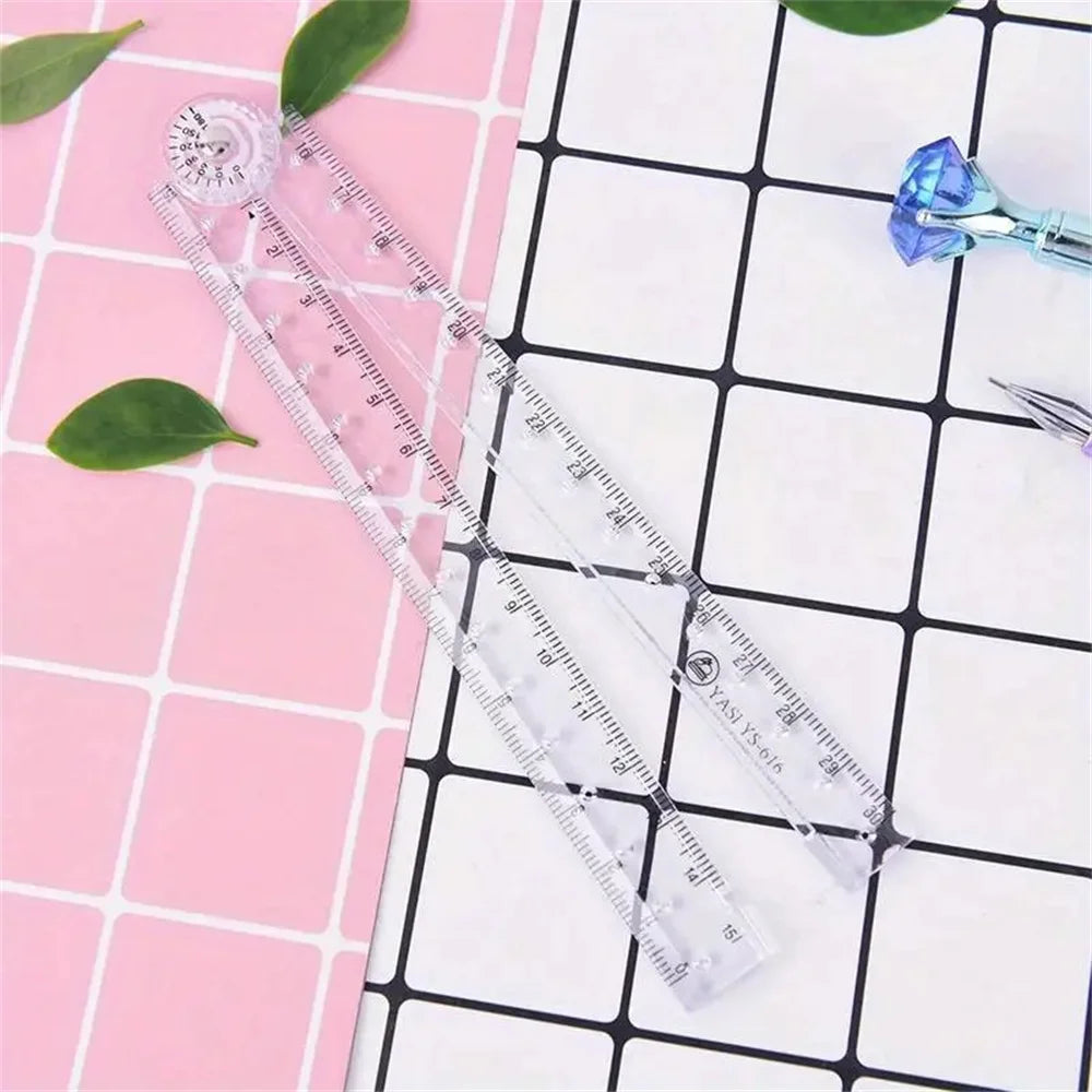 A clear acrylic folding ruler set with markings and a small blue gemstone is displayed on a pink grid background.