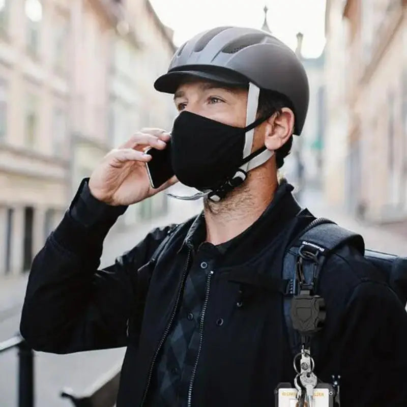 A man wearing a black jacket and helmet holds a phone to his ear while carrying a tactical ID badge holder keychain.