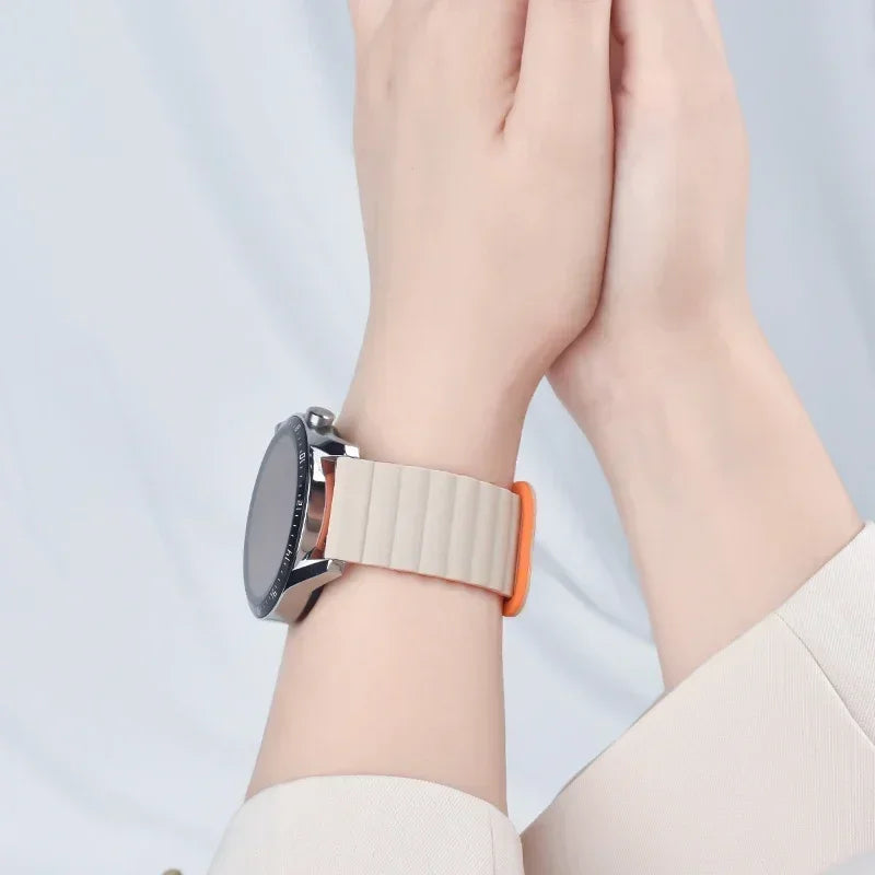 A close-up of a wrist wearing an adjustable magnetic loop watch band with a silver watch and orange accent.