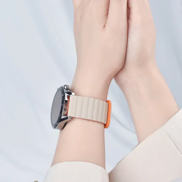 Primer plano de una muñeca con una pulsera de reloj magnética ajustable, esfera plateada y acento naranja.