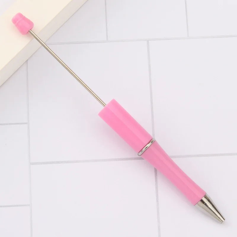 A pink DIY beadable pen with a silver tip resting on a white tiled surface.