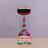 A glass hourglass filled with colored liquid, showing a transition from dark red to green and pink.
