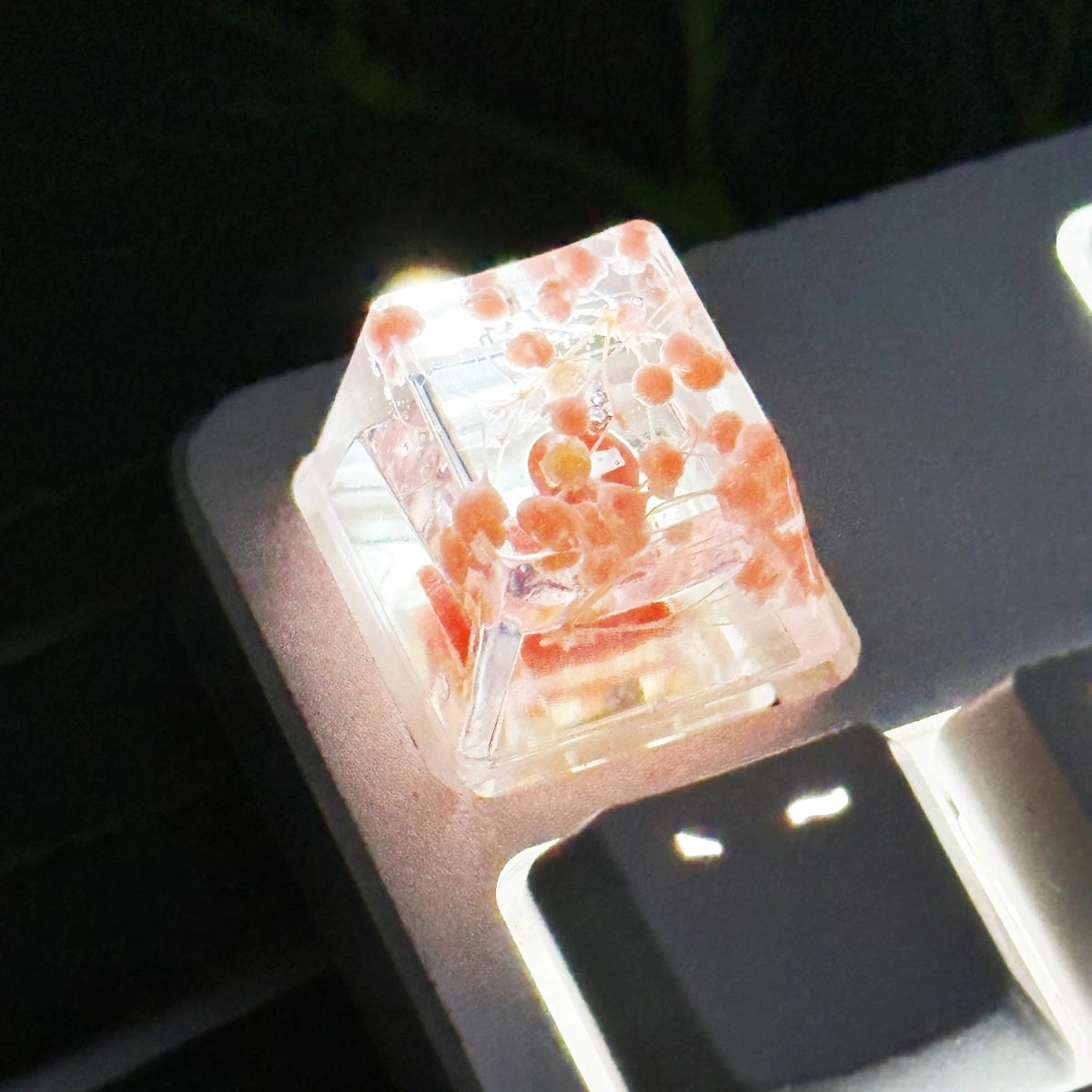 Translucent botanical resin keycaps showing pink and orange floral inclusions resting on a dark surface.