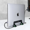 A silver laptop is supported by a black vertical stand with green cables on a white surface.