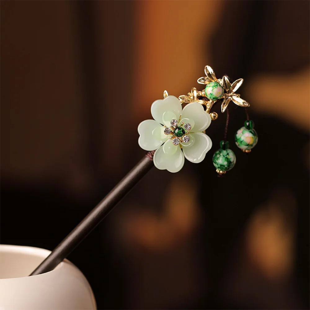 Accessoires pour cheveux floraux dorés avec des fleurs blanches et des perles vertes sur un bâton sombre.