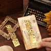 A hand holds a vintage artistic metal bookmark with a gold tassel resting on a wooden surface.