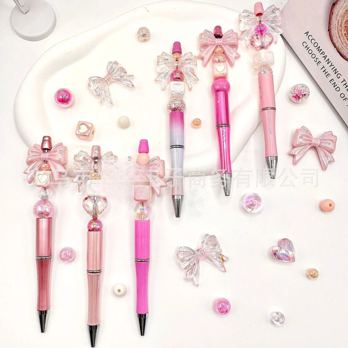 A set of pink and iridescent gradient acrylic beaded pens displayed on a white surface.