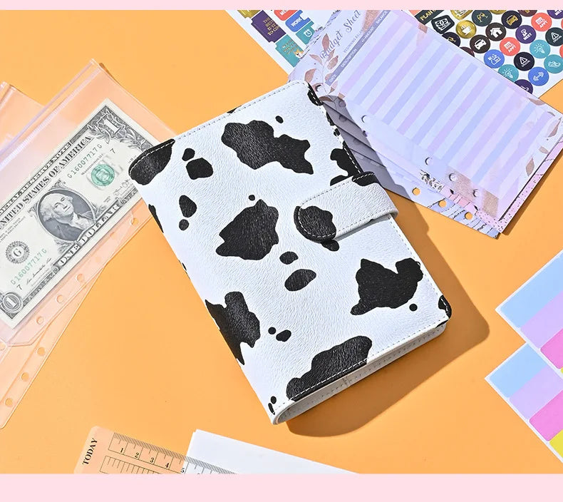 A white leather A6 binder with a black leopard print design next to stacks of pink and purple paper.