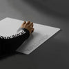 Une main pose un tapis de souris en verre blanc avec l'inscription WALLHACK sur une surface gris foncé.