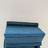 A teal foldable tablet pillow stand with a pocket is held in a hand against a plain background.