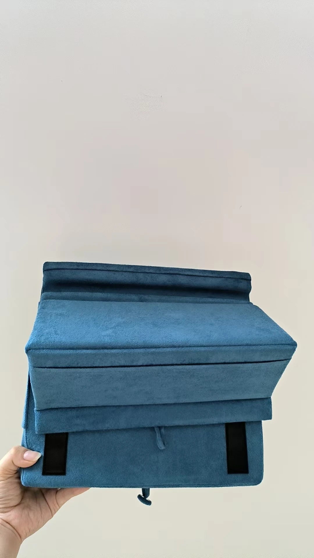 A teal foldable tablet pillow stand with a pocket is held in a hand against a plain background.