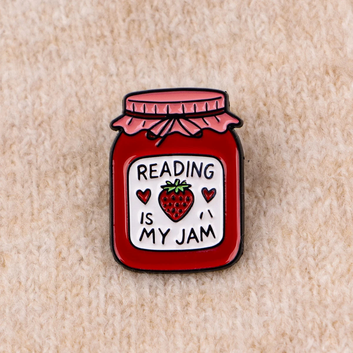 Red enamel lapel pin shaped like a jar of strawberry jam with the text Reading is my jam on the label