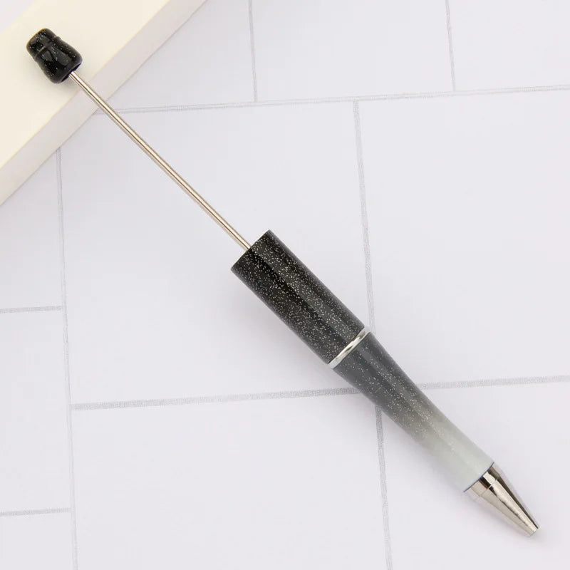 A black DIY beadable pen set with a silver tip is shown lying on a white surface.