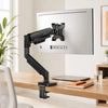 A black monitor arm is mounted on a wooden desk, positioned above a laptop and notebook.