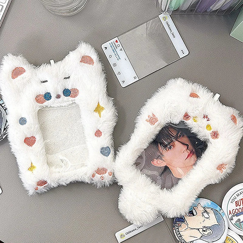 A white fluffy cat-shaped plush holder with colorful hearts and stars, used to display a K-pop photocard.
