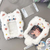 A white fluffy cat-shaped plush holder with colorful hearts and stars, used to display a K-pop photocard.