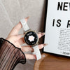 A hand holds a white resin beaded watch with a black face and silver accents against a blurred background.