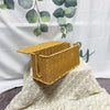 A handwoven rattan cable management box with a lid in a golden yellow color resting on a white lace fabric.