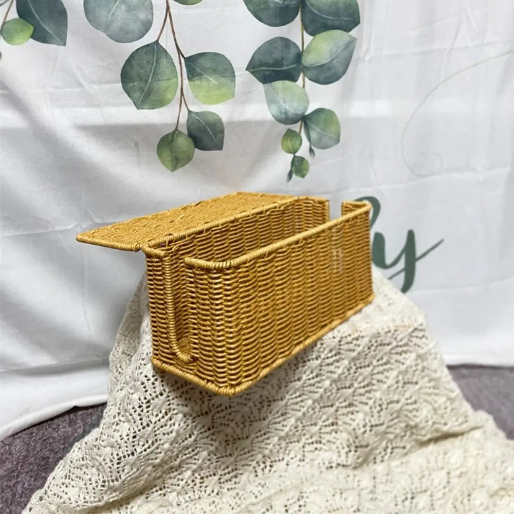 A handwoven rattan cable management box with a lid in a golden yellow color resting on a white lace fabric.