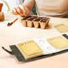 A wooden serving board displays a tart filled with dark seeds and a set of labeled seed storage cards.