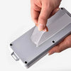 A hand applies a piece of clear double-sided adhesive tape to a gray rectangular product.