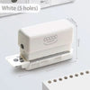 A white mini multi-hole punch tool with five holes is shown next to a stack of paper.