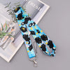A blue and yellow cartoon cat print lanyard with a metal clasp is displayed next to some greenery on a white background.