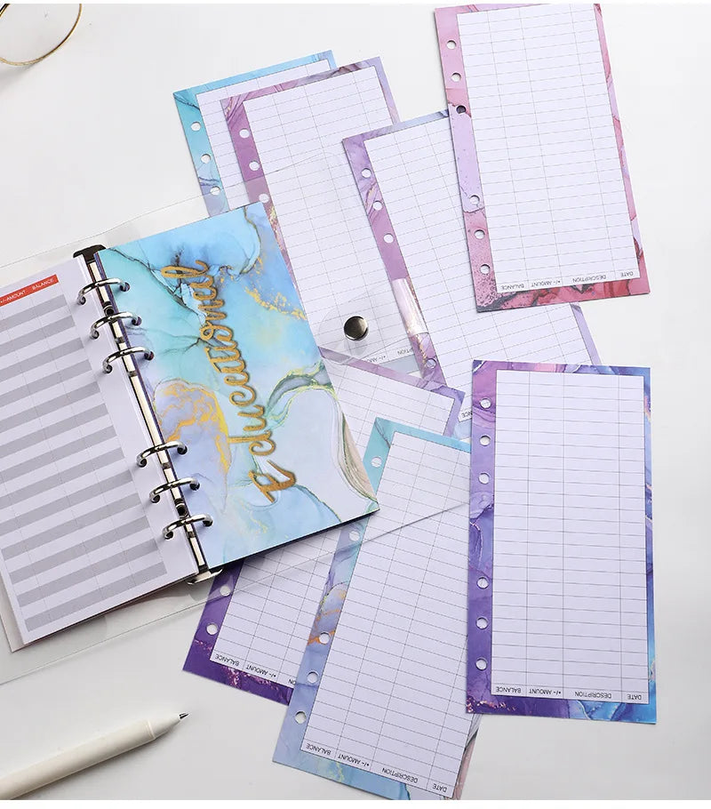 A stack of A6 budget planner binders with pink and blue marbled covers and grid paper pages.