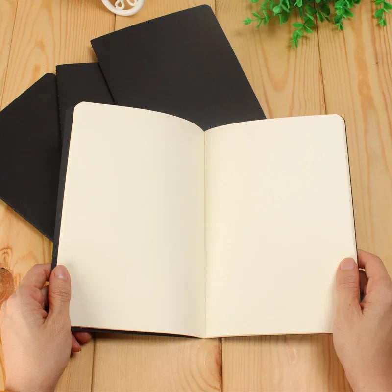 A blank A6 sketchbook with cream-colored pages is open, resting on a wooden surface.