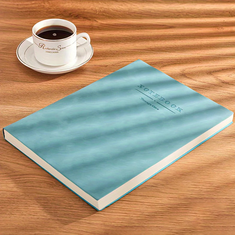 A light blue notebook lying on a wooden surface next to a white cup and saucer.
